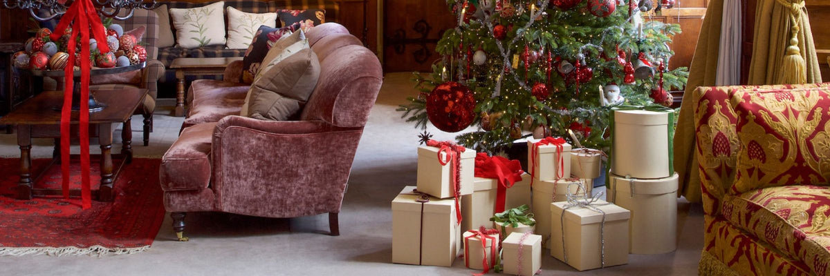 A cozy holiday living room scene with a pink velvet armchair, a decorated Christmas tree, wrapped gift boxes, and warm-toned furniture.