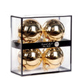Four shiny gold glass Christmas ornaments 10 cm diameter, inside a clear rectangular display box with a black frame and a black band label reading 'Goodwill M&G Co. Glass Baubles'. Photographed on a white backgraund 