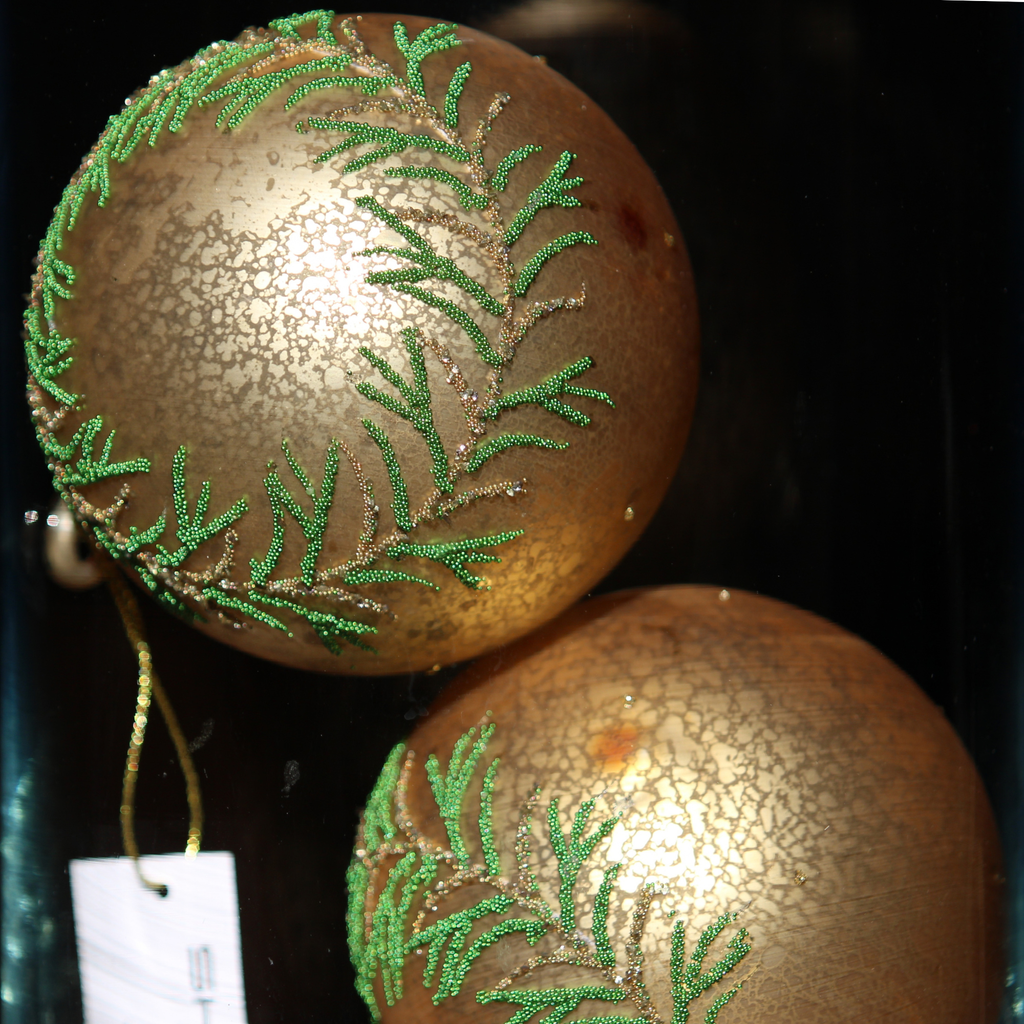 Two round gold Christmas ornaments with a crackled metallic finish and green beaded leaf patterns, shown close up against a dark background.