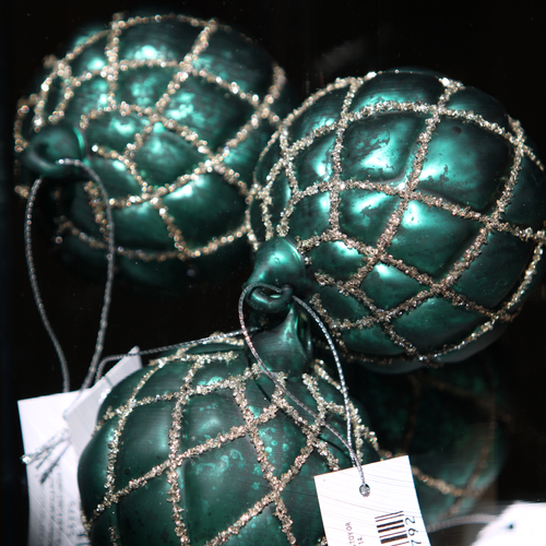Three metallic teal green Christmas ornaments with a glittery silver lattice pattern, shown with retail tags against a dark background.