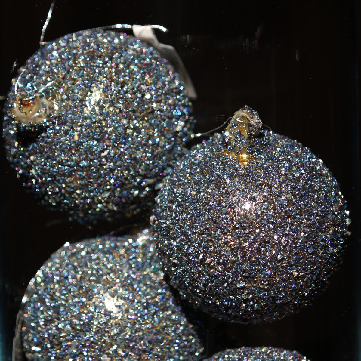 Three round glitter Christmas ornaments in a dark iridescent blue-purple color, covered in fine holographic glitter with small gold hanging loops, shown against a black background.