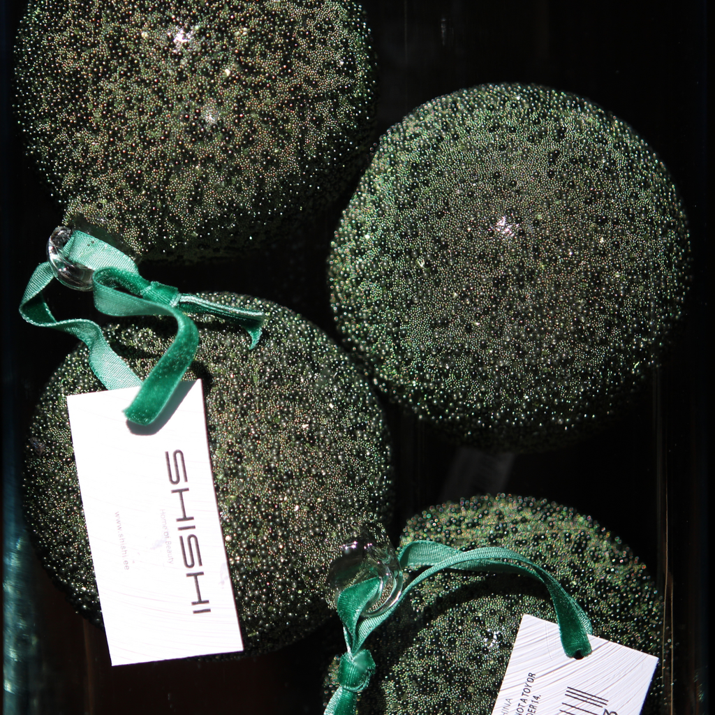 Four round green glitter Christmas ornaments with shiny green ribbons and white tags printed with the brand name 'ISHII', displayed against a dark background.
