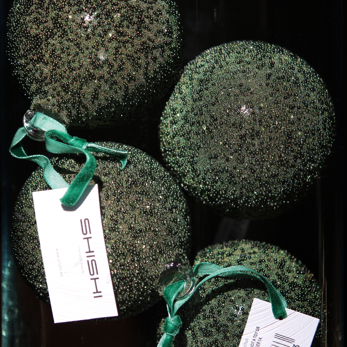 Four round green glitter Christmas ornaments with shiny green ribbons and white tags printed with the brand name 'ISHII', displayed against a dark background.