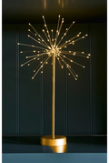 A gold-colored table lamp with a spherical burst of warm white LED fairy lights on a slim pole and round base, set against a dark paneled background.