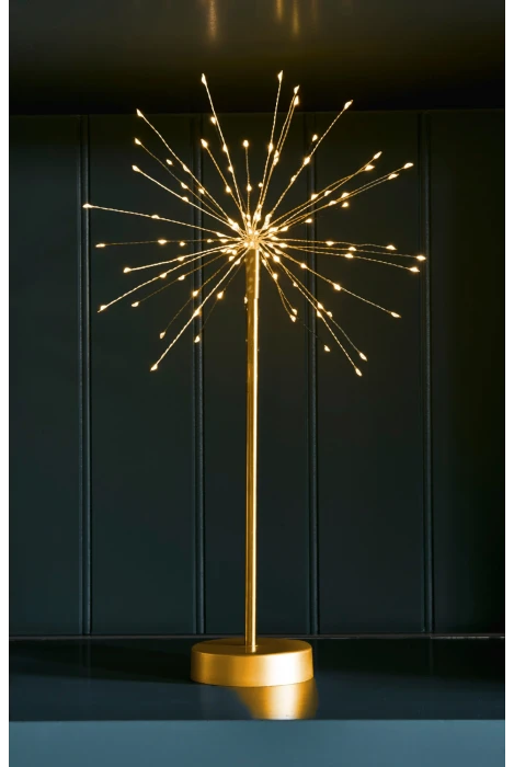 A gold-colored table lamp with a spherical burst of warm white LED fairy lights on a slim pole and round base, set against a dark paneled background.