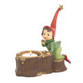 A Christmas helper pixie figurine kneeling beside a tree stump candle holder, wearing a red pointed hat with a gold star, a green outfit, and red shoes, set against a plain white background - 16 cm