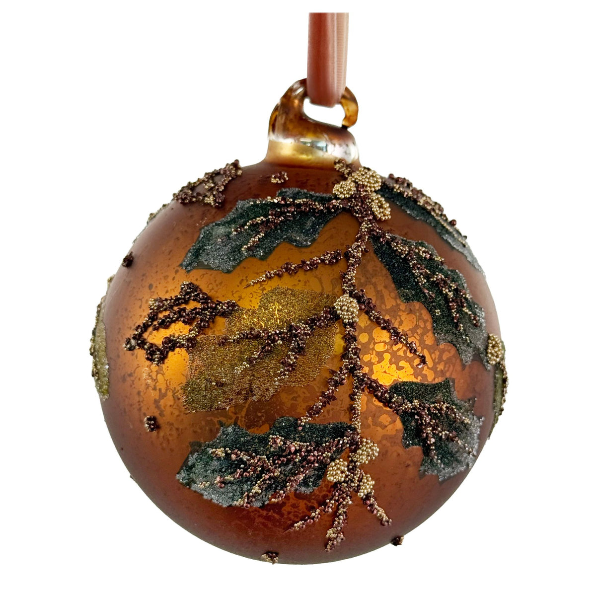A round amber glass Christmas ornament decorated with metallic gold glitter, dark green leaf accents, and small brown bead details, hanging from a brown ribbon against a white background.